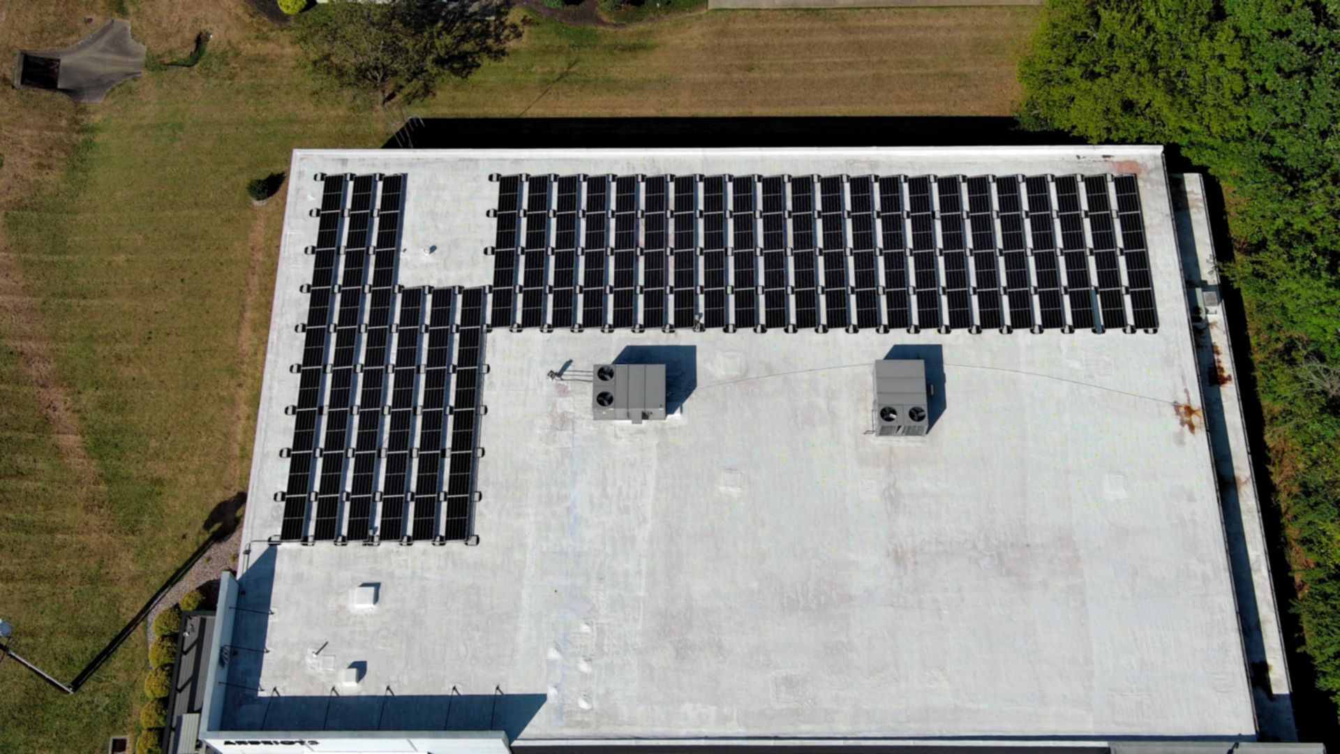 Aerial view of a flat rooftop with solar panels along one edge and two small rooftop units.