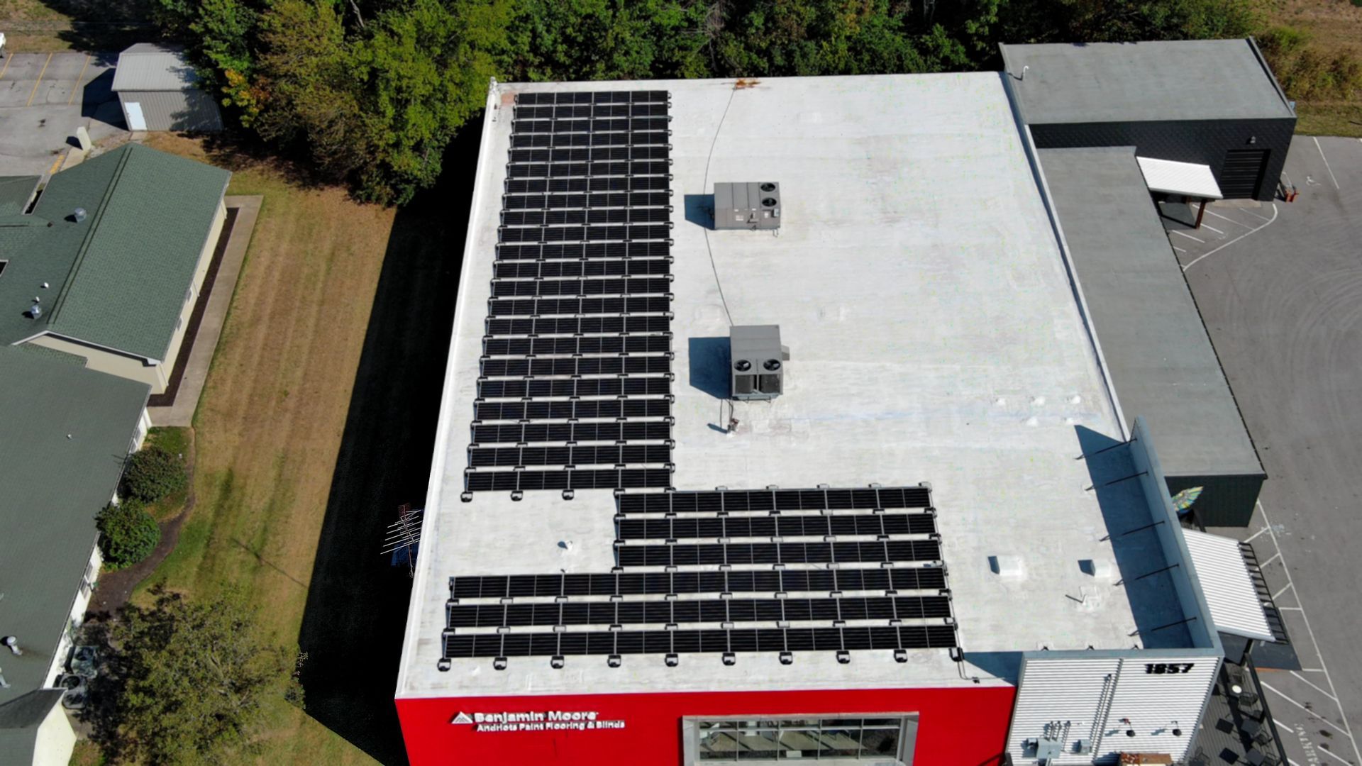 Aerial view of a building roof covered with solar panels. Red wall visible with the words 