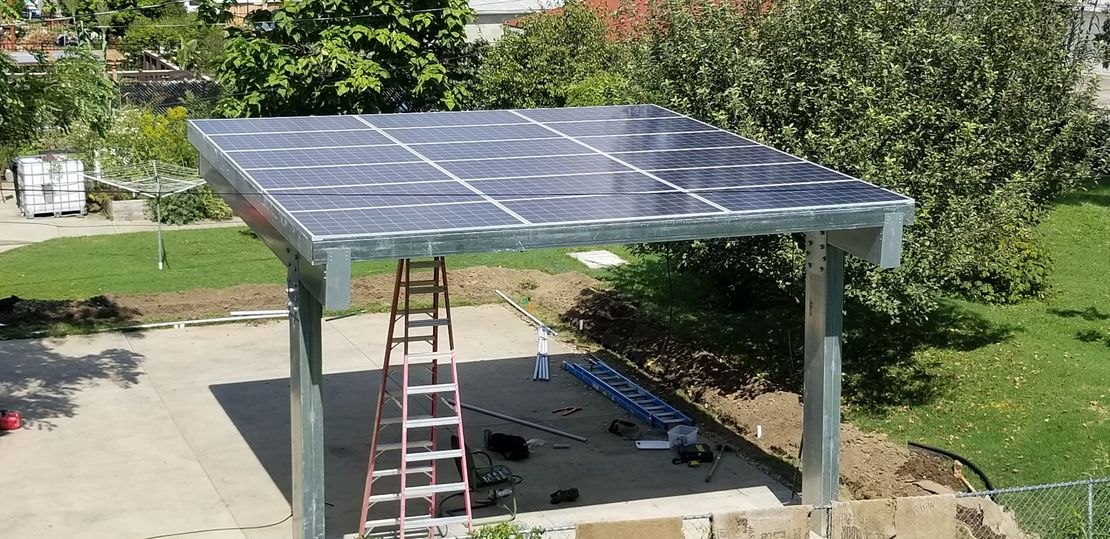 Solar panels on a carport-style canopy with a ladder underneath in a backyard.