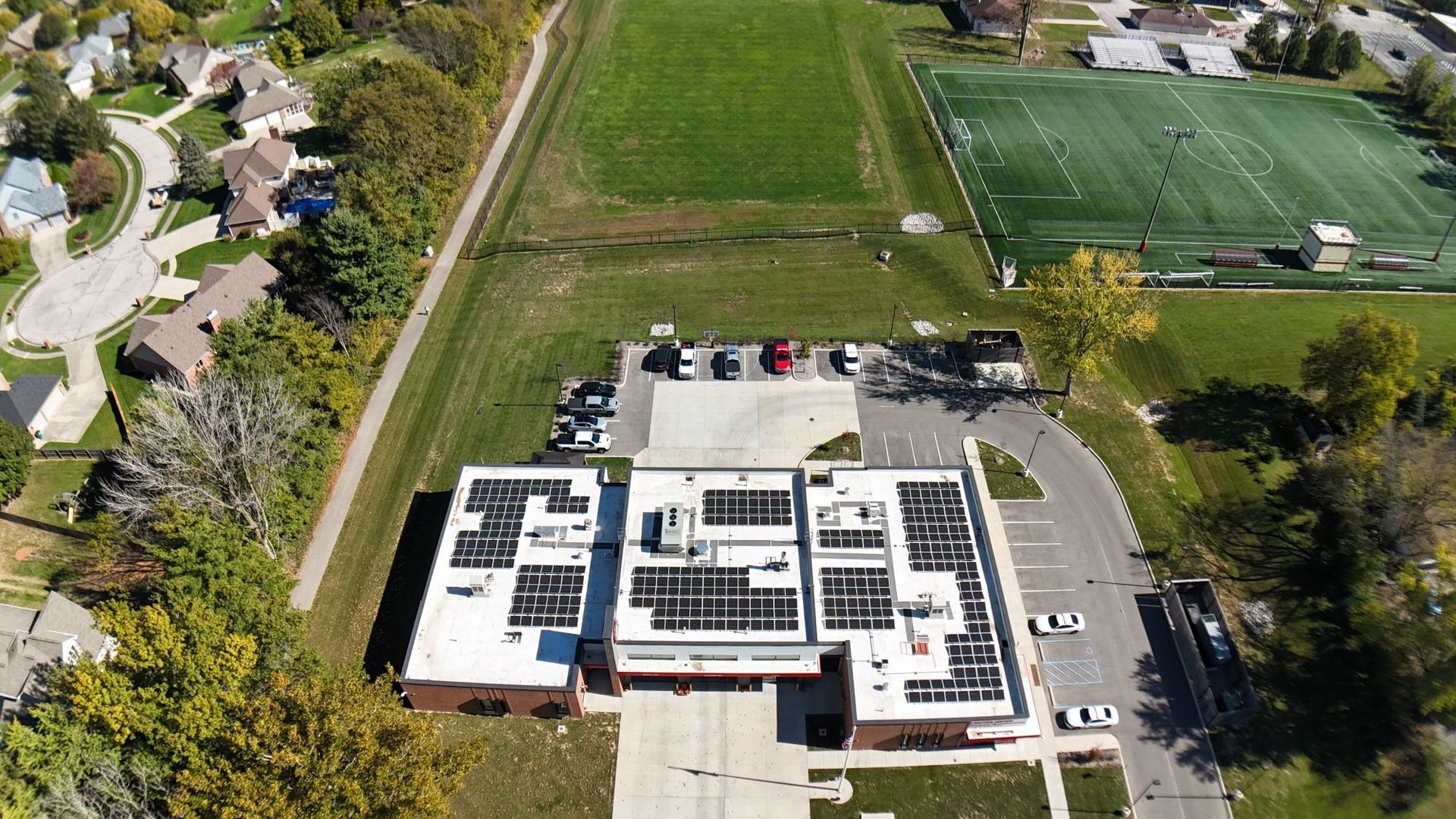 Aerial view of a school building with solar panels on the roof, a parking lot, and a grassy field.