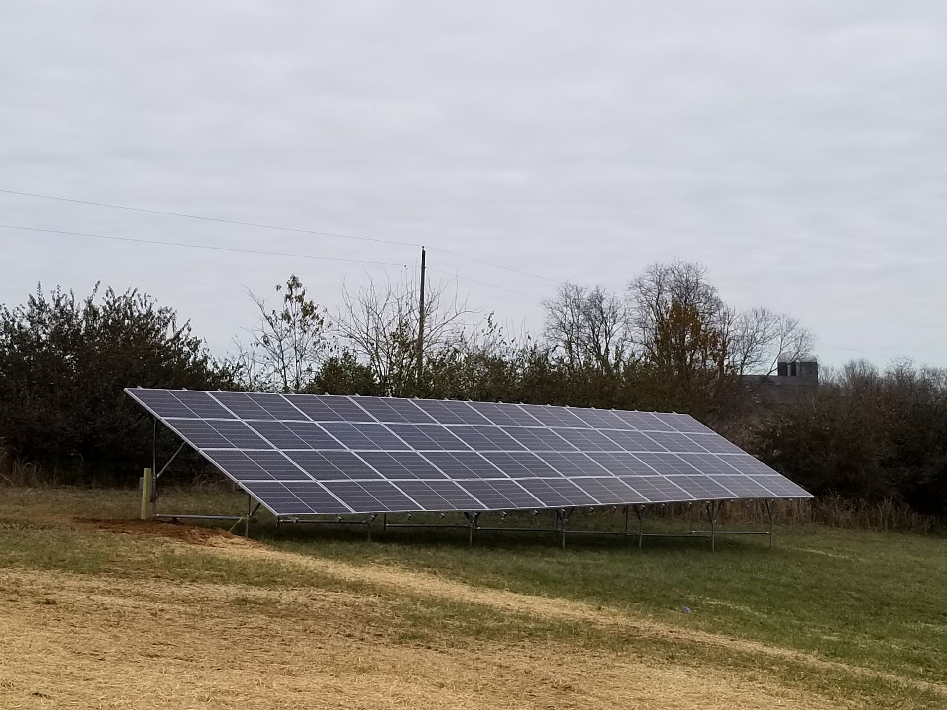 Solar panel array on a grassy field under a cloudy sky.