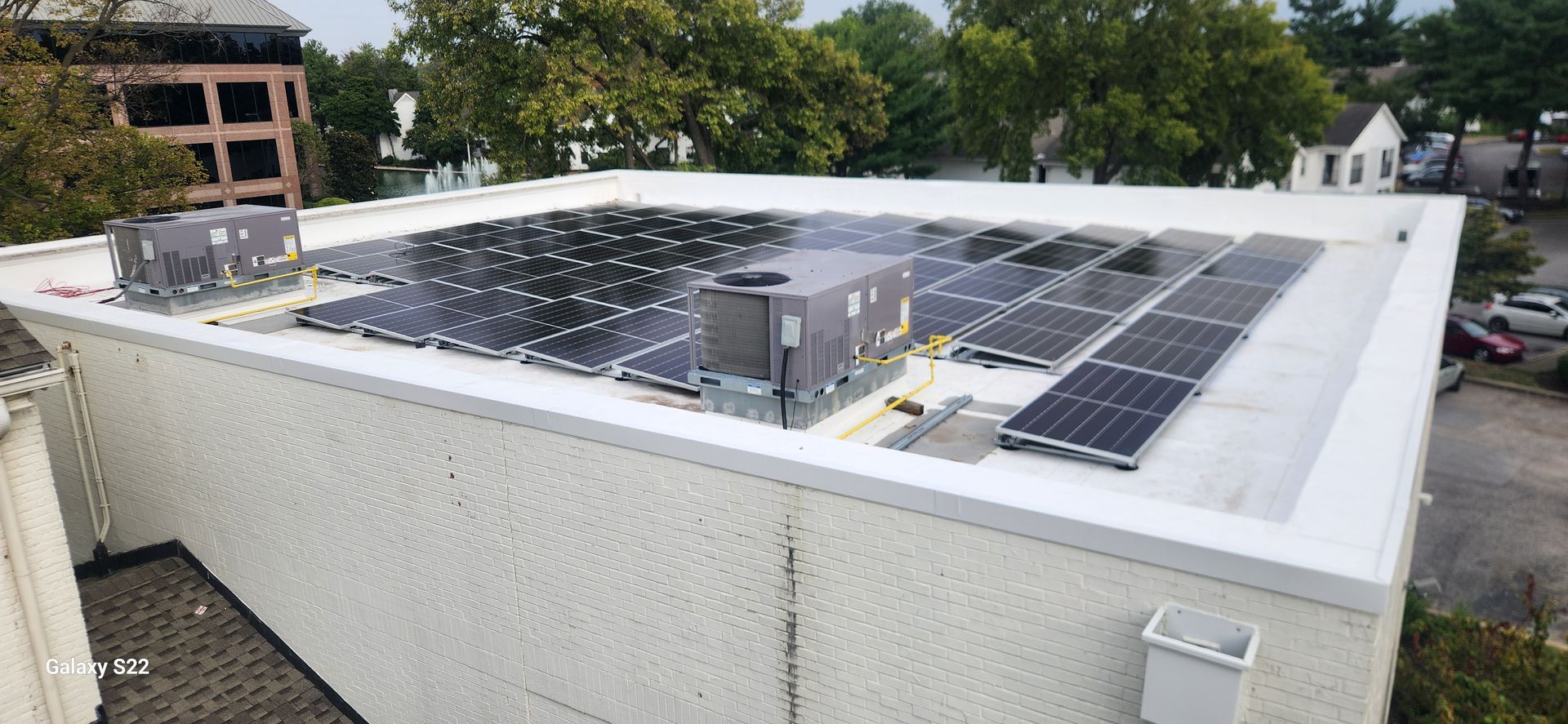 Rooftop solar panels on a building. White walls and roof, with trees in the background.