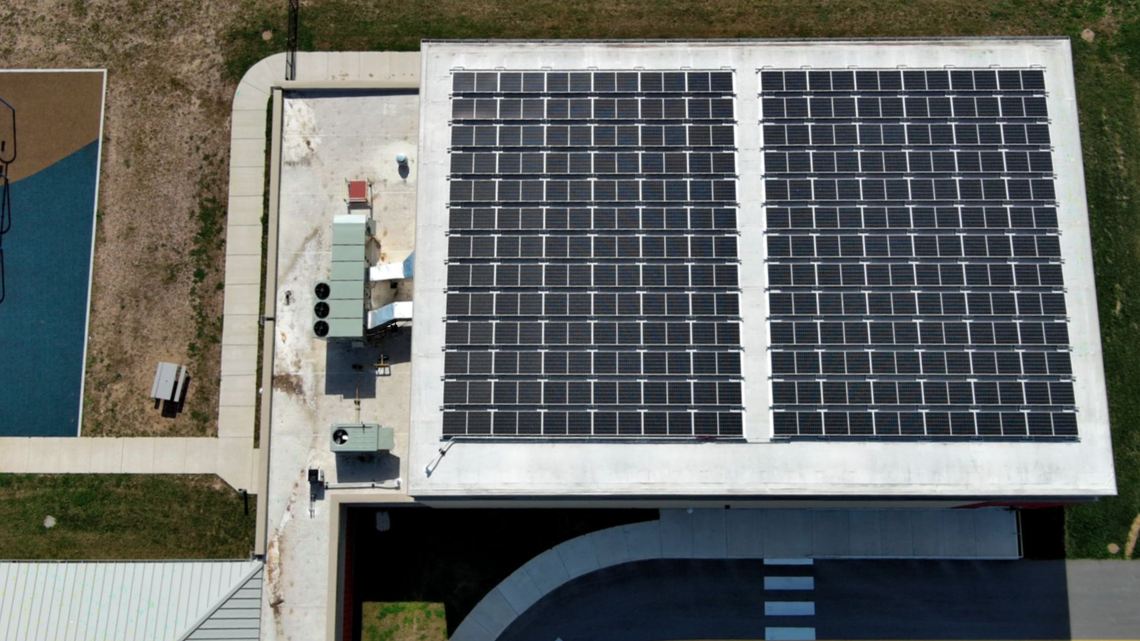 Aerial view of a building rooftop covered with solar panels beside a street and sidewalk.