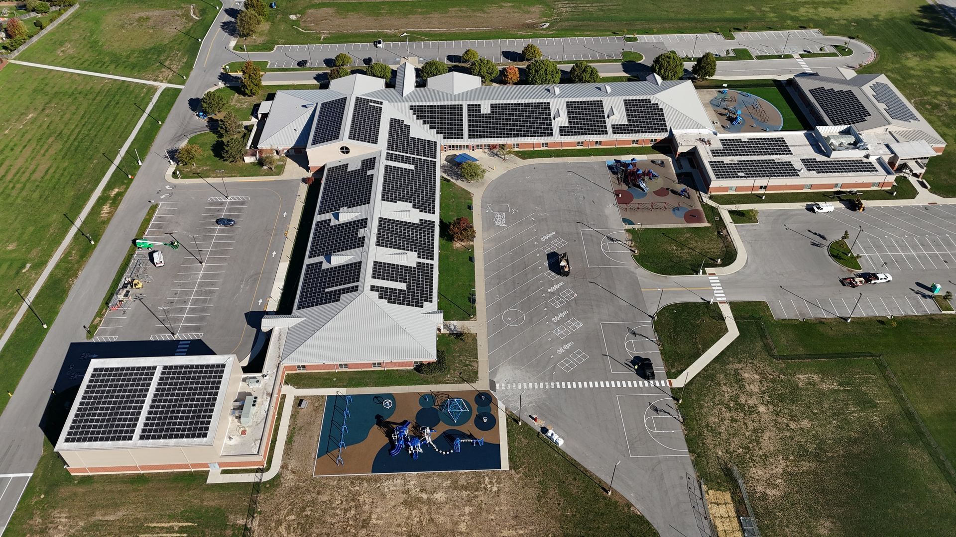 Aerial view of a school building with solar panels on the roof, a playground, and a parking lot.