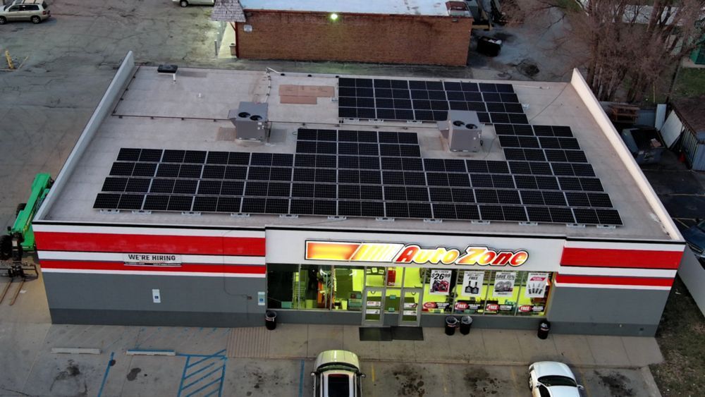 A convenience store with solar panels on the roof. Exterior shot with red and white signage and cars parked in front.