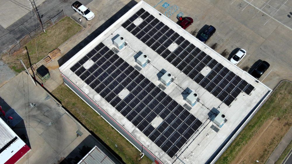 Aerial view of a building roof with solar panels, air conditioning units, and parked cars.