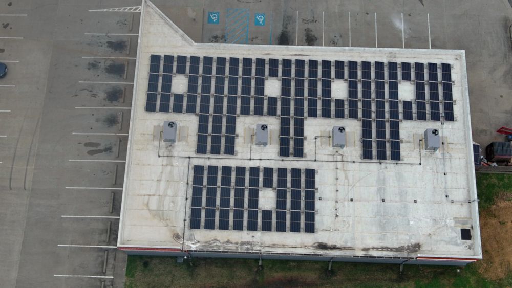 Overhead view of a building roof covered in solar panels, some with square cutouts.