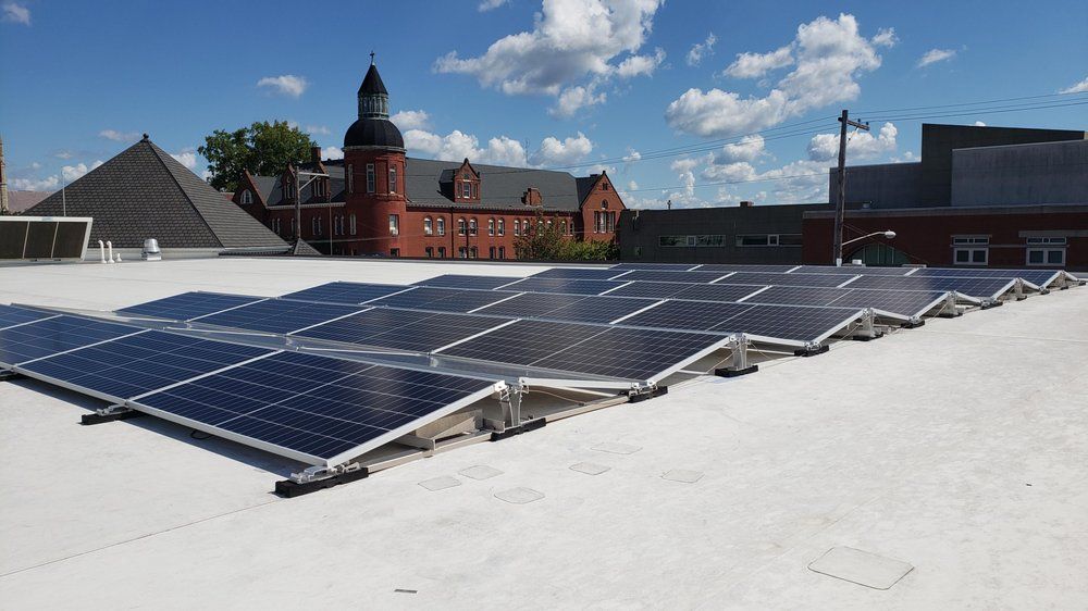 Solar panels on a white roof with a brick building and blue sky in the background.