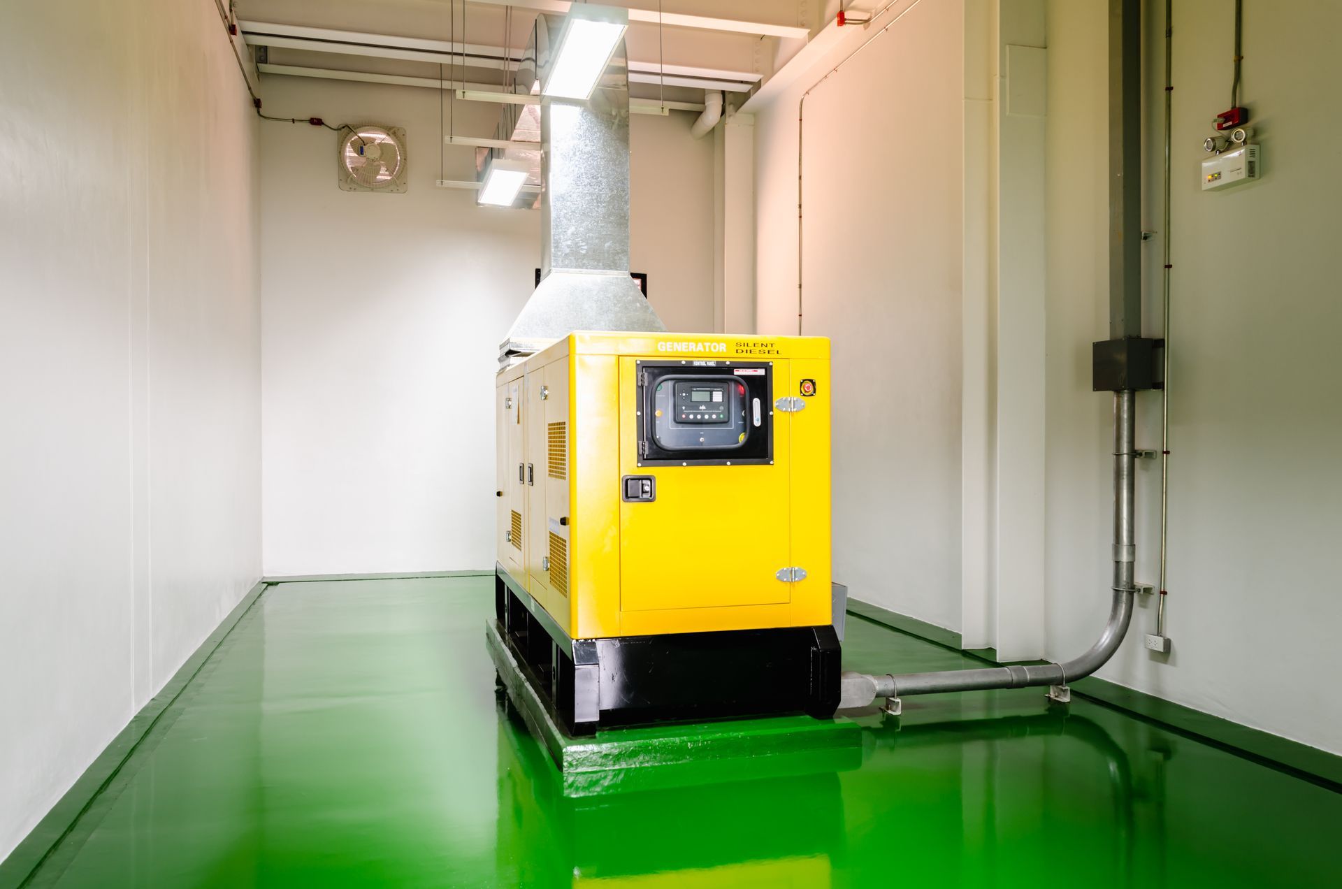 Yellow generator in a small room with green floor and white walls, with an exhaust pipe.