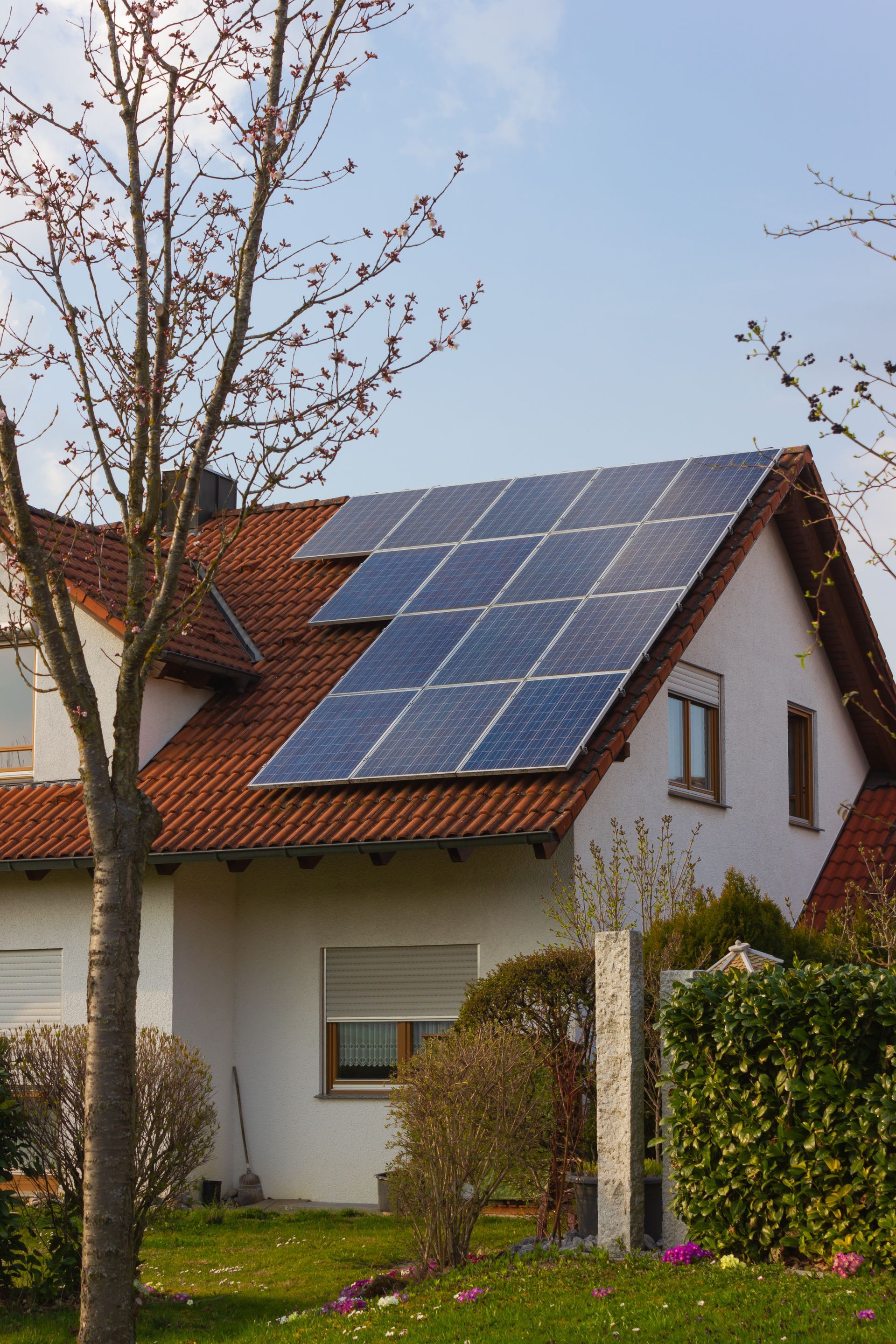 House with solar panels on a red-tiled roof in a suburban yard
