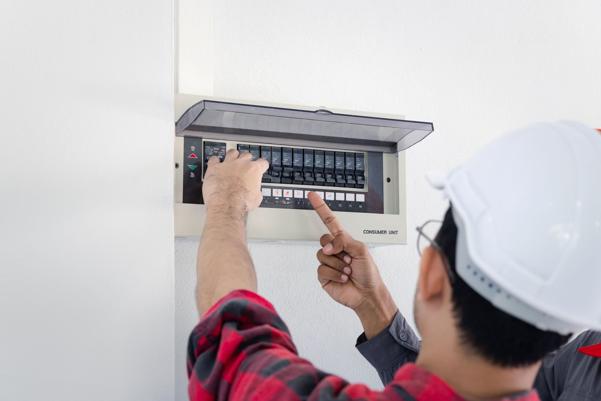 Electrician in a white helmet working on a circuit breaker panel indoors.