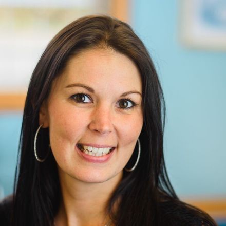 Smiling woman with dark hair and hoop earrings against a softly blurred background