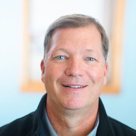 Smiling man in a dark polo against a softly blurred light blue background