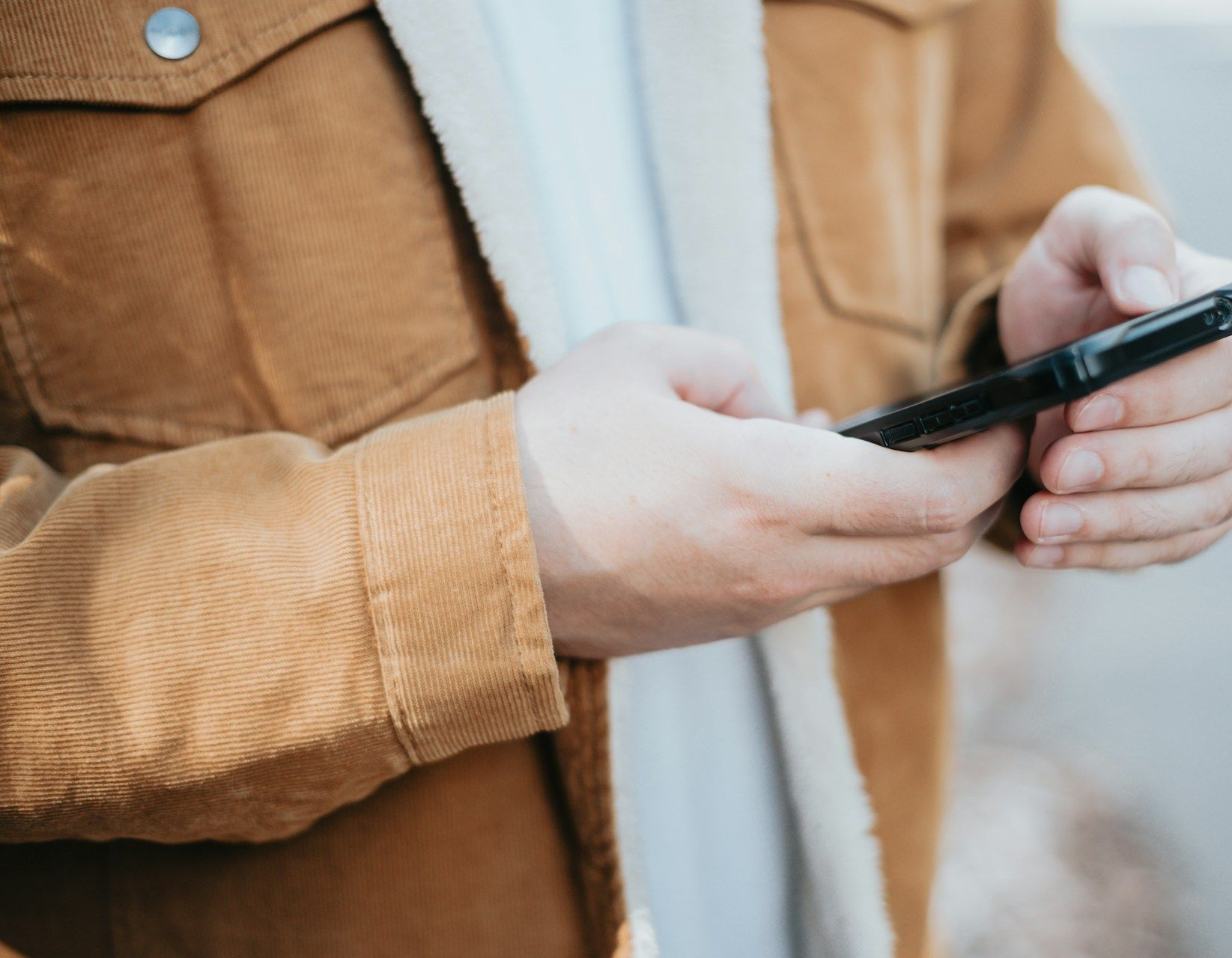 Close-up of hands holding a black pen and a smartphone, wearing a brown jacket.