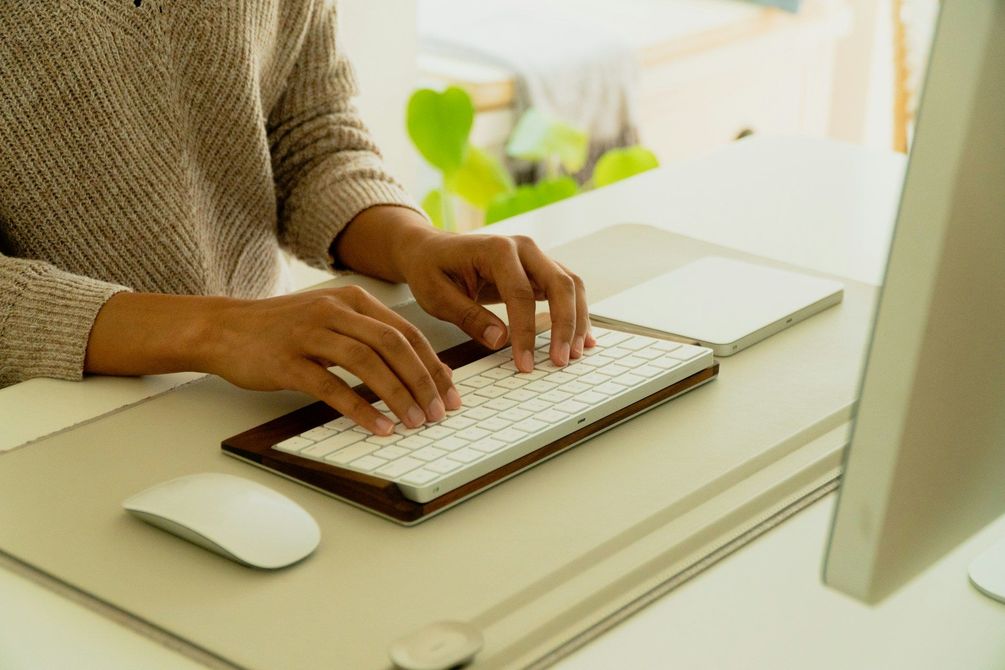 Hands typing on a white keyboard at a desk beside a monitor and mouse.