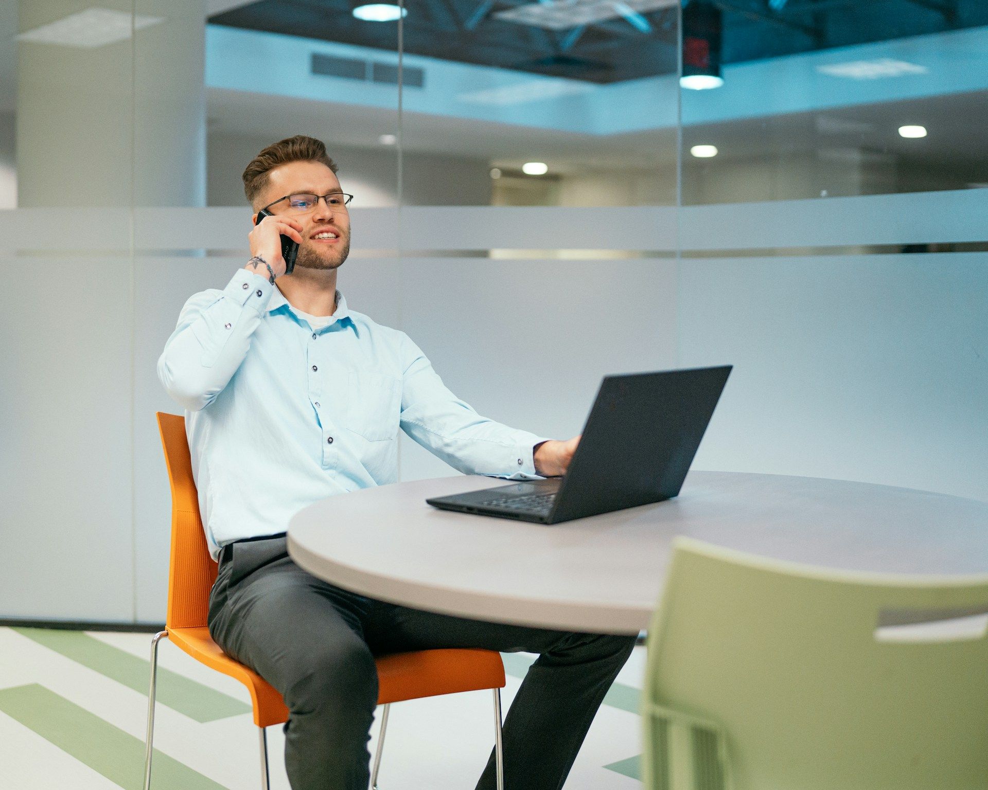 Person on a phone call at a table with a laptop in a modern office lounge