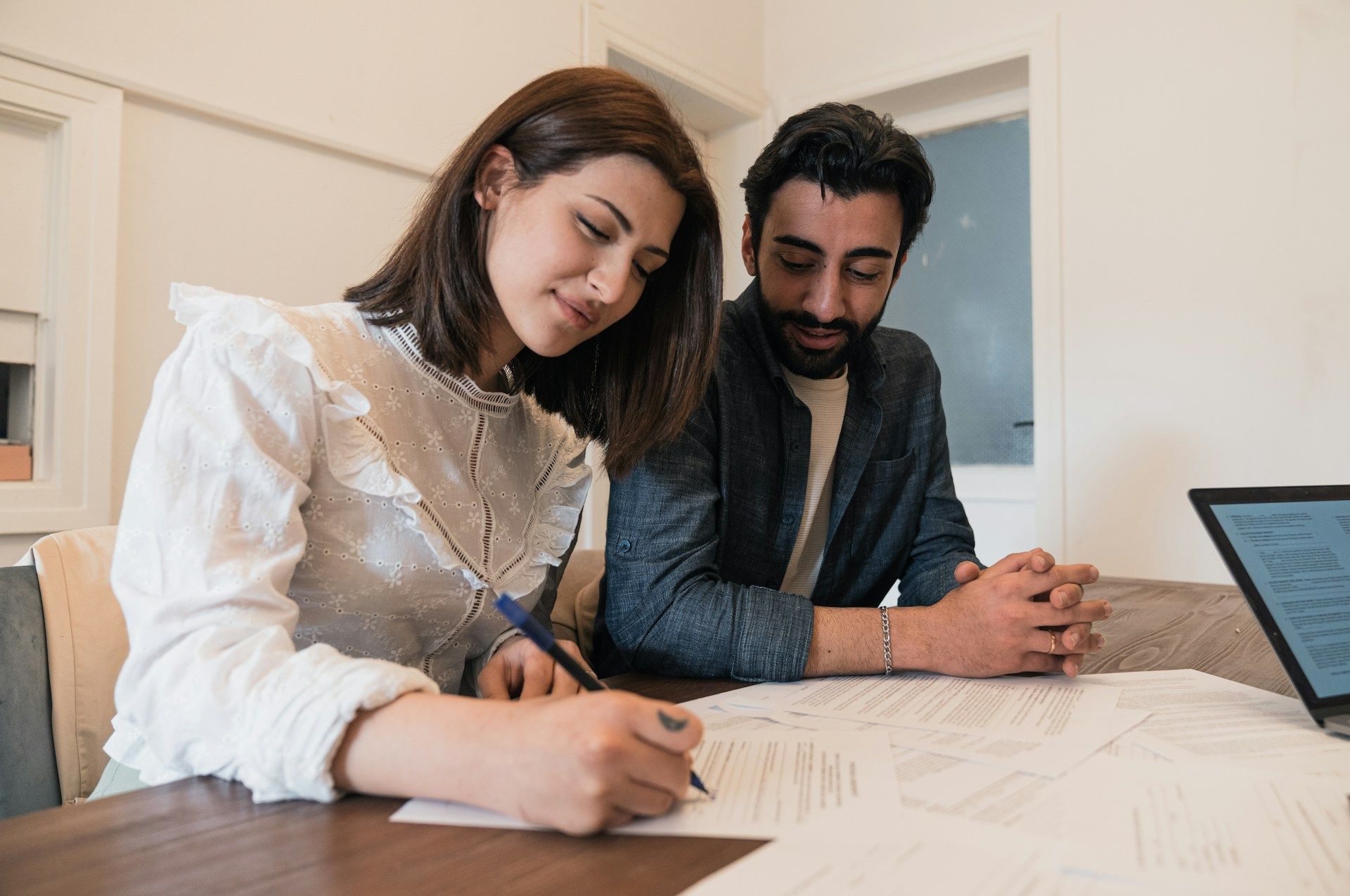 Two people reviewing documents at a desk, with a laptop in a bright office