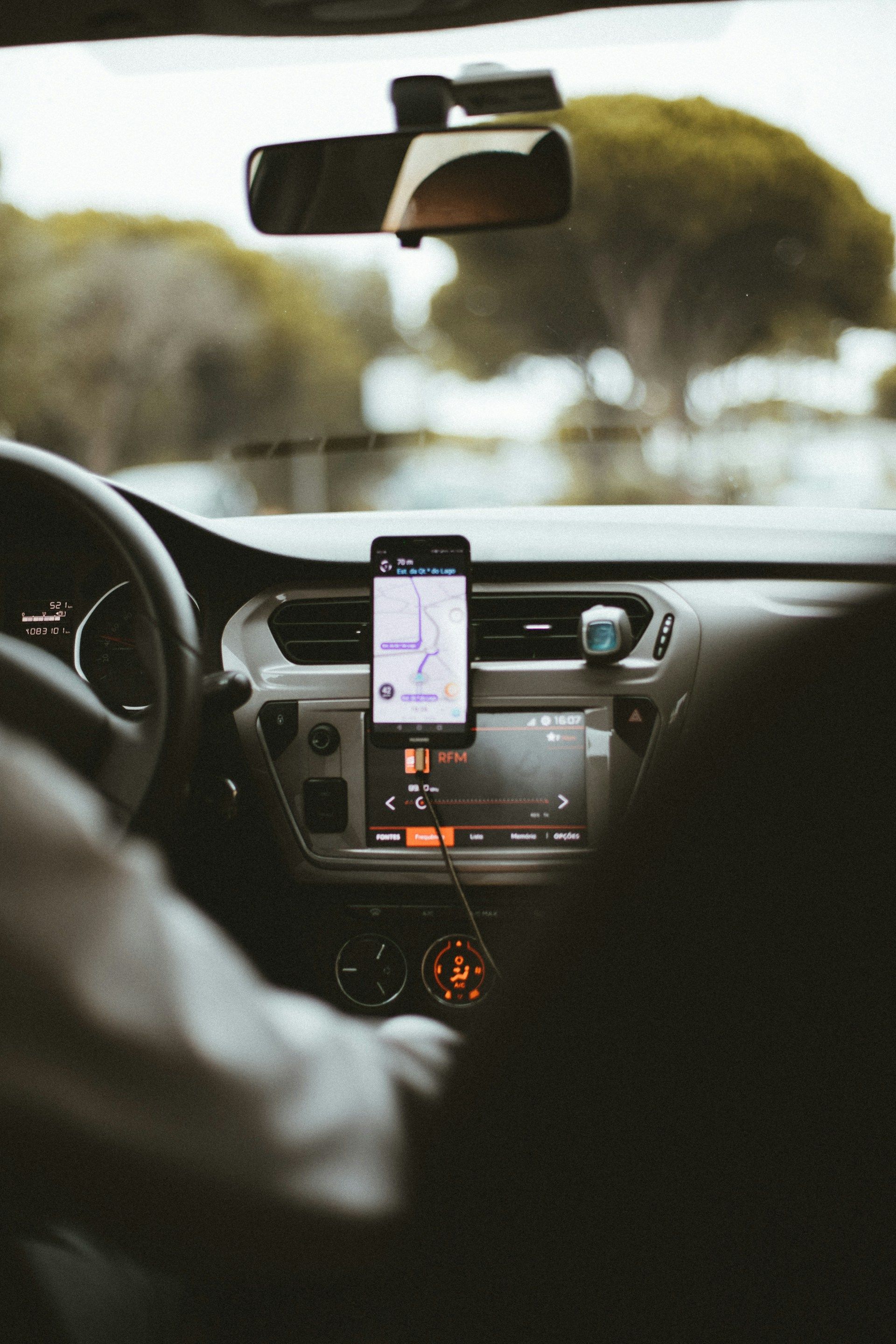 Inside a car, a driver uses a smartphone mounted on the dashboard, with a blurred road ahead.