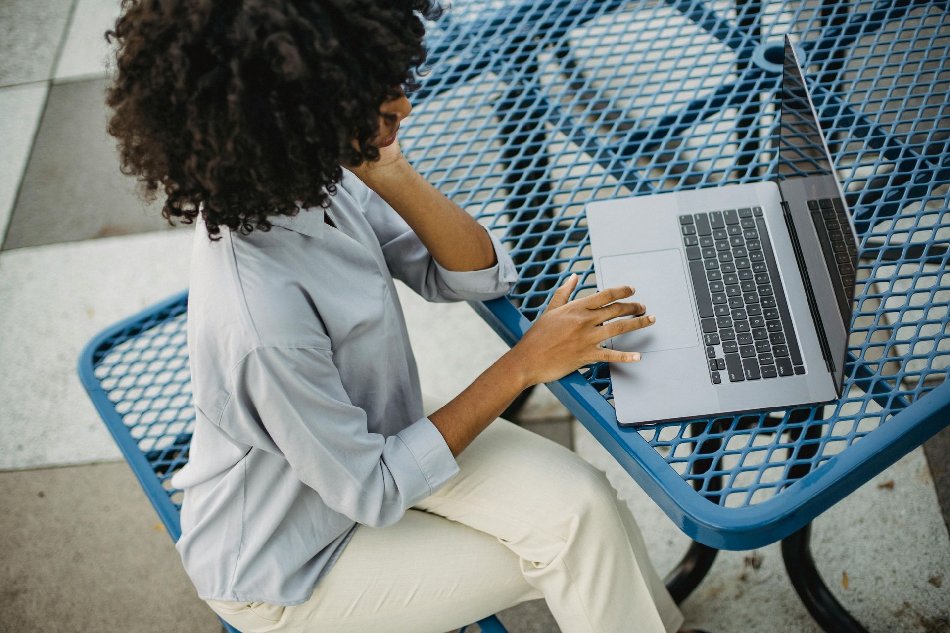 Person working on a laptop at a blue outdoor table on a tiled patio
