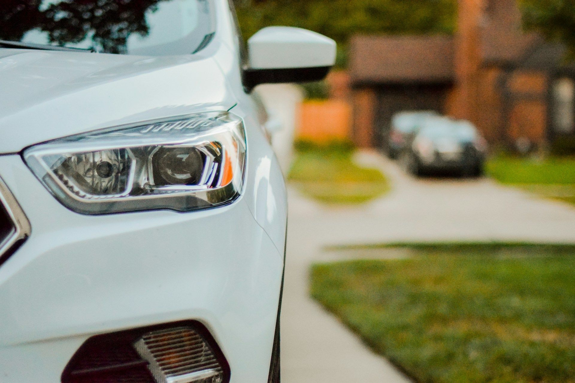White car front end parked by a suburban curb with a headlight in close-up