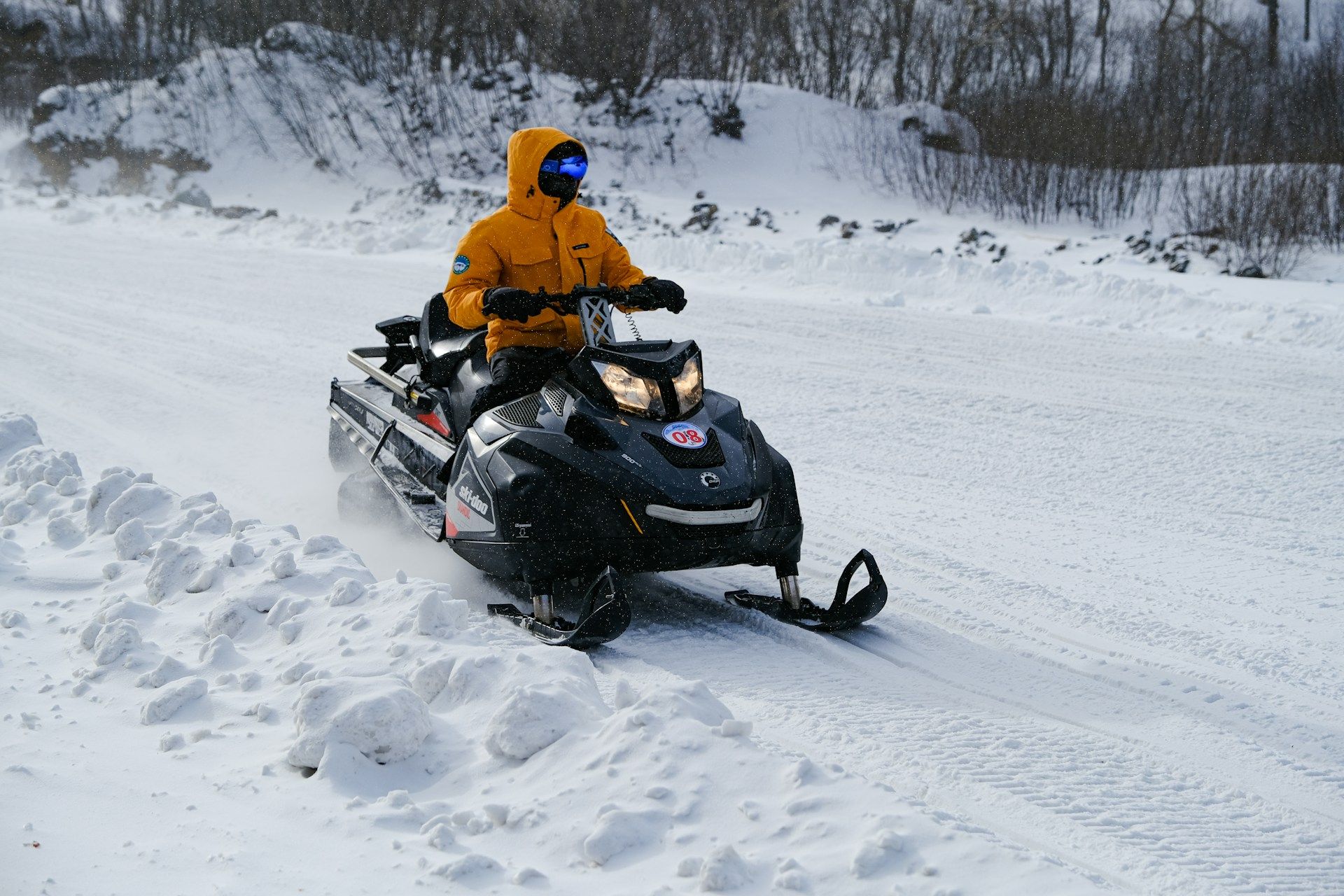 Person in orange jacket riding a black snowmobile on a snowy trail