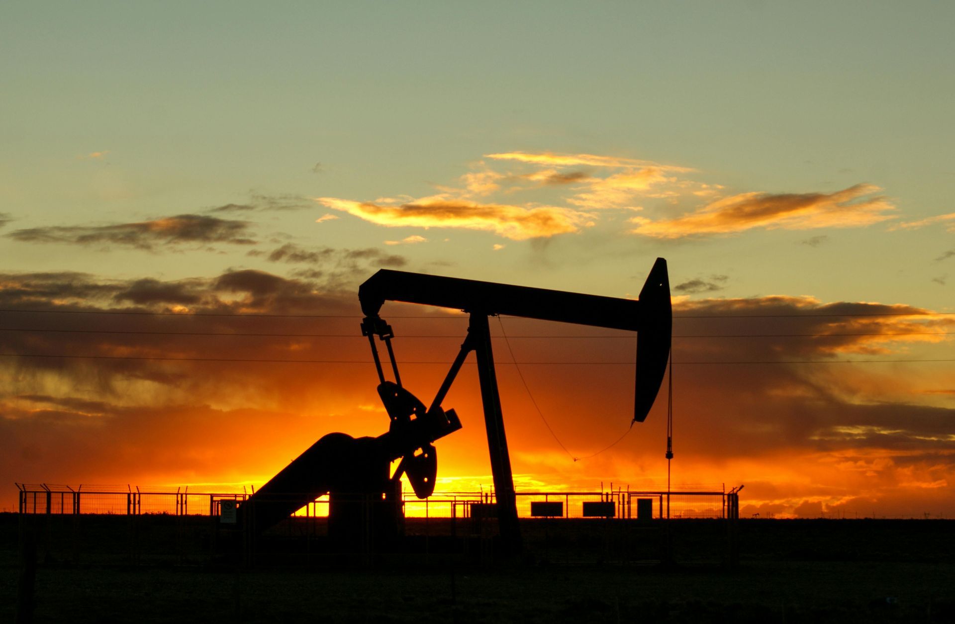 An oil pump is silhouetted against a sunset sky