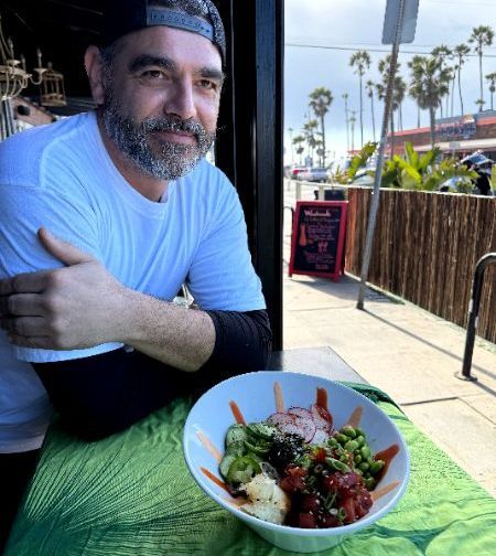 A man is sitting at a table with a bowl of Poke.