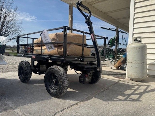 Black utility trailer with large tires loaded with boxes under a covered outdoor area