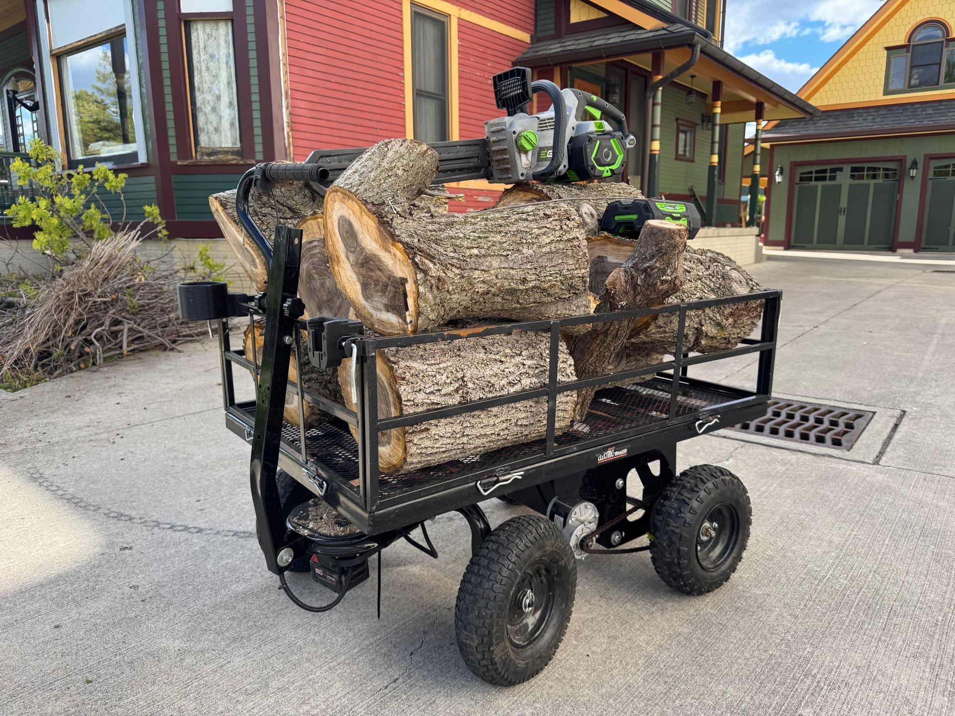 Loaded utility cart with large cut logs outside a house
