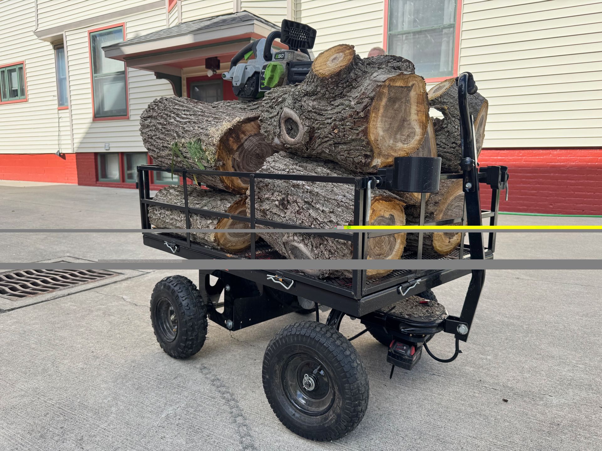 Utility cart loaded with cut wood logs parked beside a building
