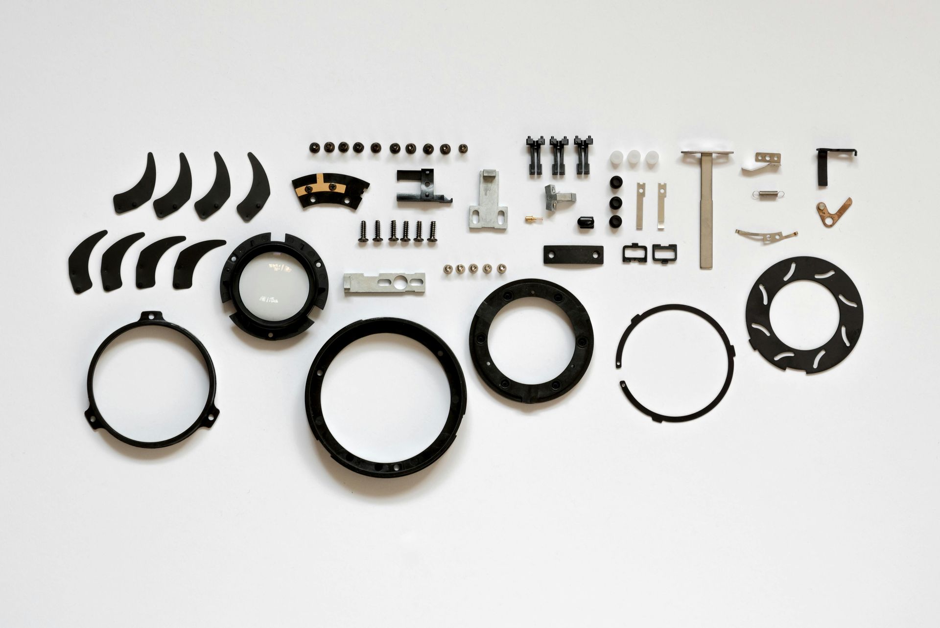 Parts of a camera lens, disassembled and laid out on a white surface.