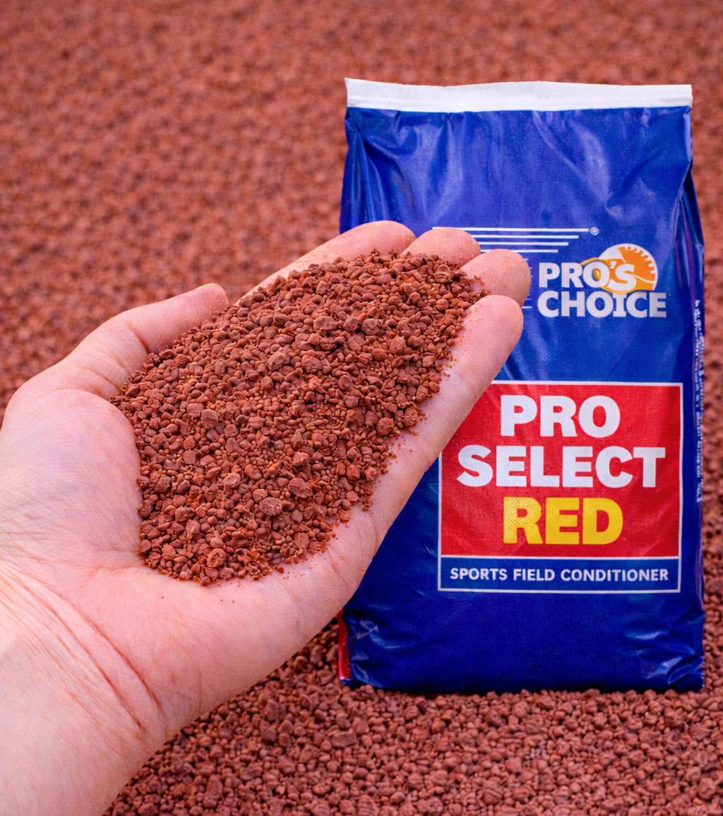 Hand holding red granules in front of a blue bag labeled “PRO SELECT RED” sports field conditioner