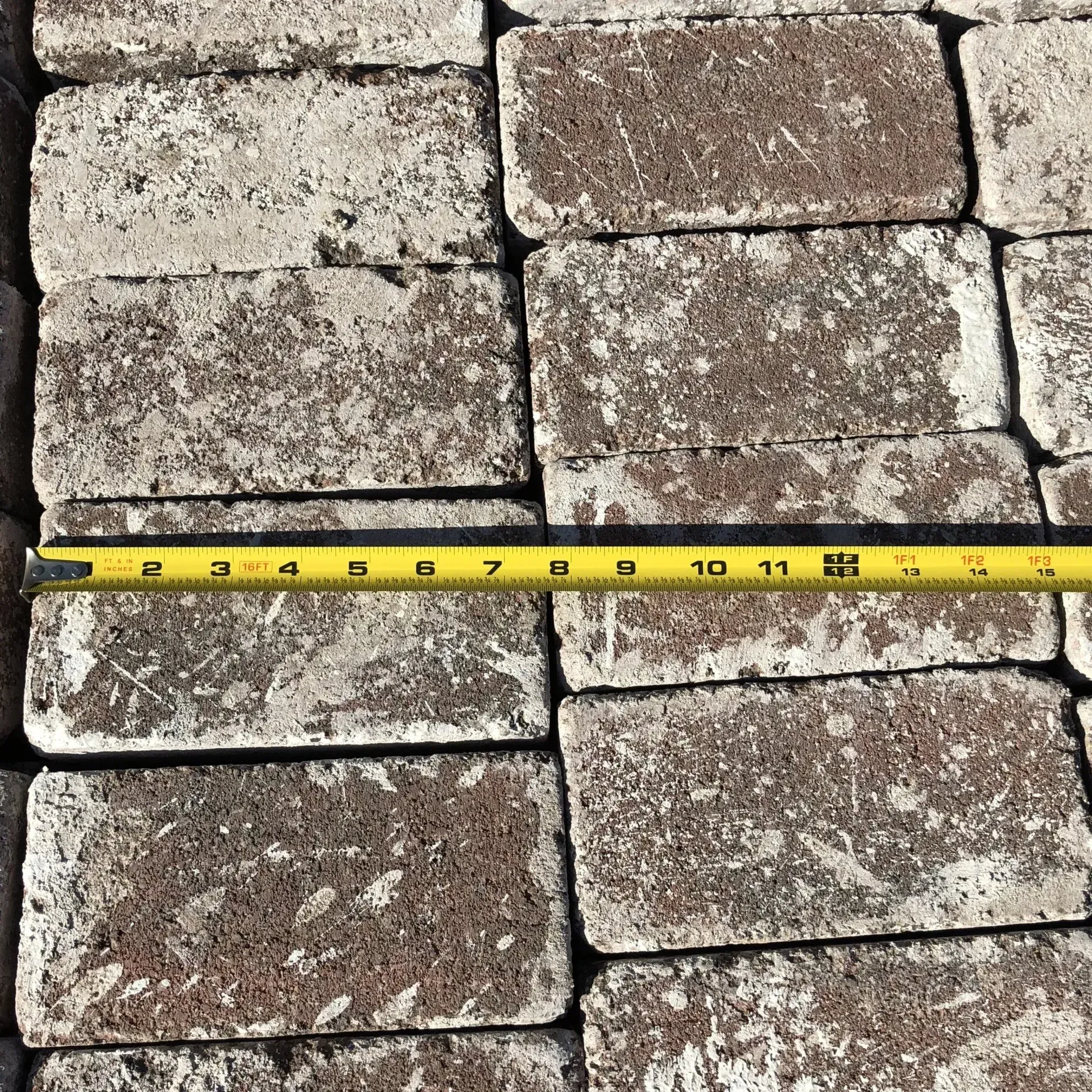 Measuring tape stretched across weathered stone pavers on the ground