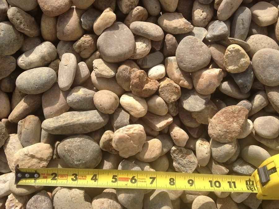 Close-up of mixed tan and gray pebbles with a yellow measuring tape along the bottom edge.