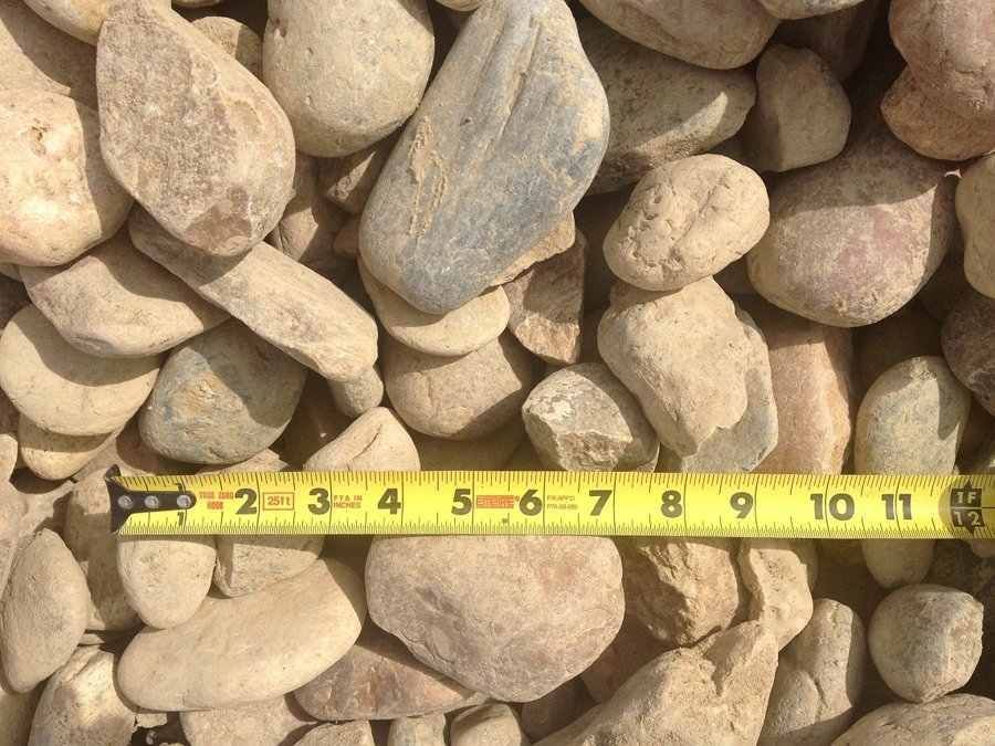 Pile of tan river rocks with a yellow measuring tape stretched across the bottom.