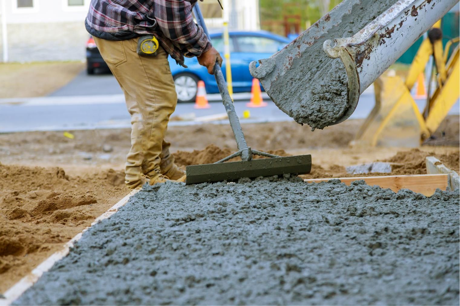 Worker smoothing wet concrete with a rake as fresh concrete is poured at a construction site.