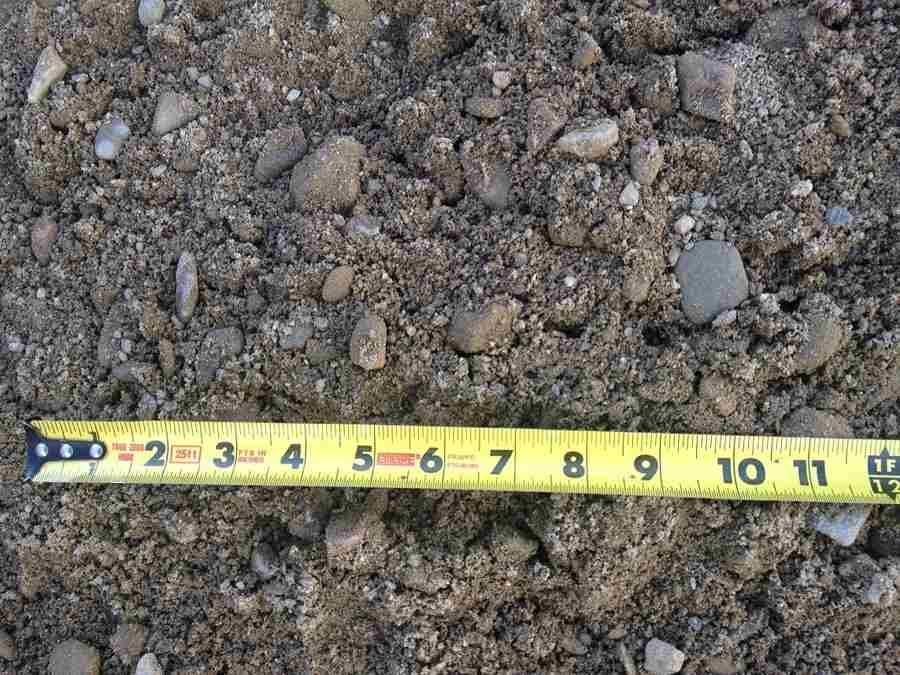 Yellow measuring tape over gravel and small rocks, marked with inches 2 to 11.
