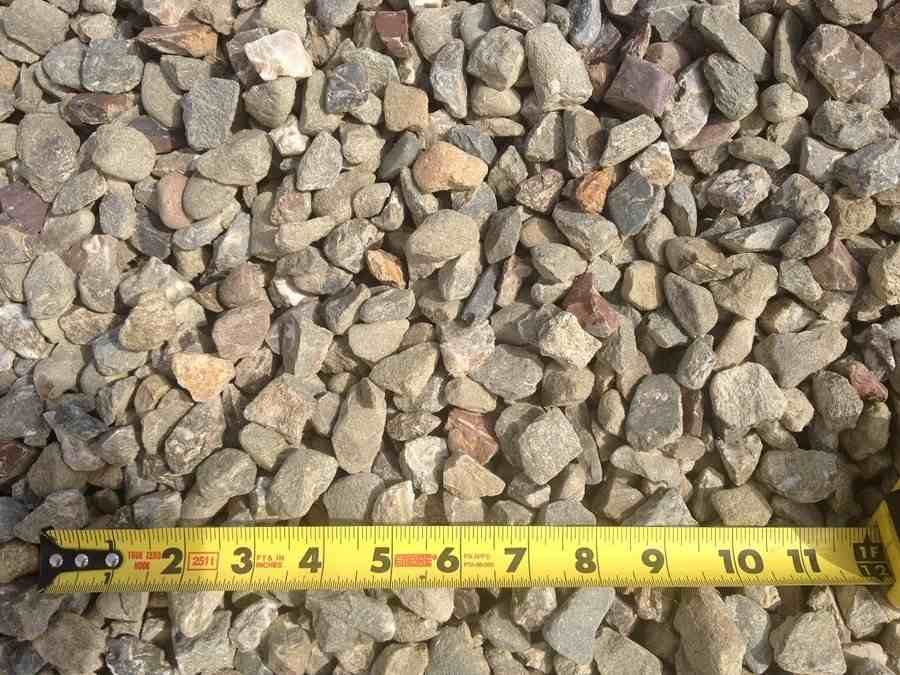 Pile of small gray and tan gravel with a yellow measuring tape along the bottom edge