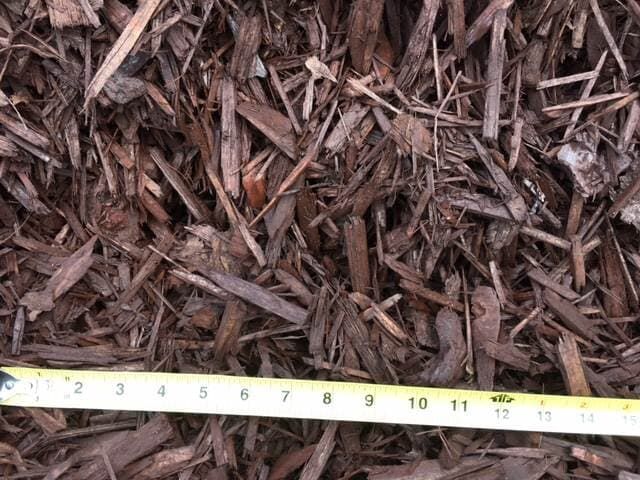Brown wood chips mulch with a yellow measuring tape along the bottom edge.