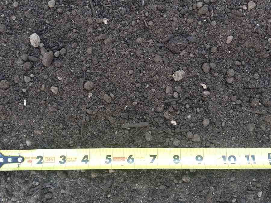 Close-up of dark gravel soil with a yellow measuring tape along the bottom edge.