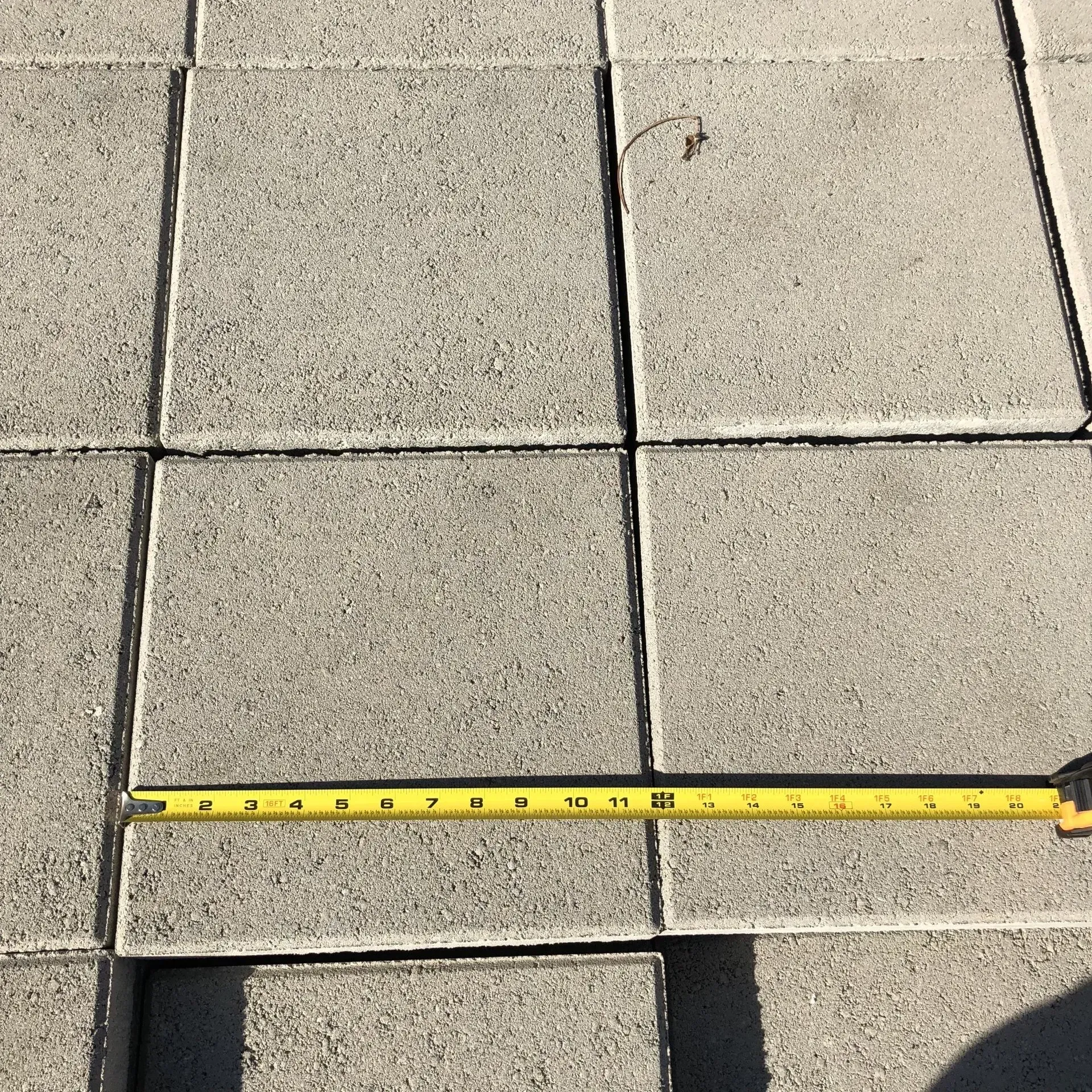 Yellow measuring tape laid across gray concrete patio tiles.
