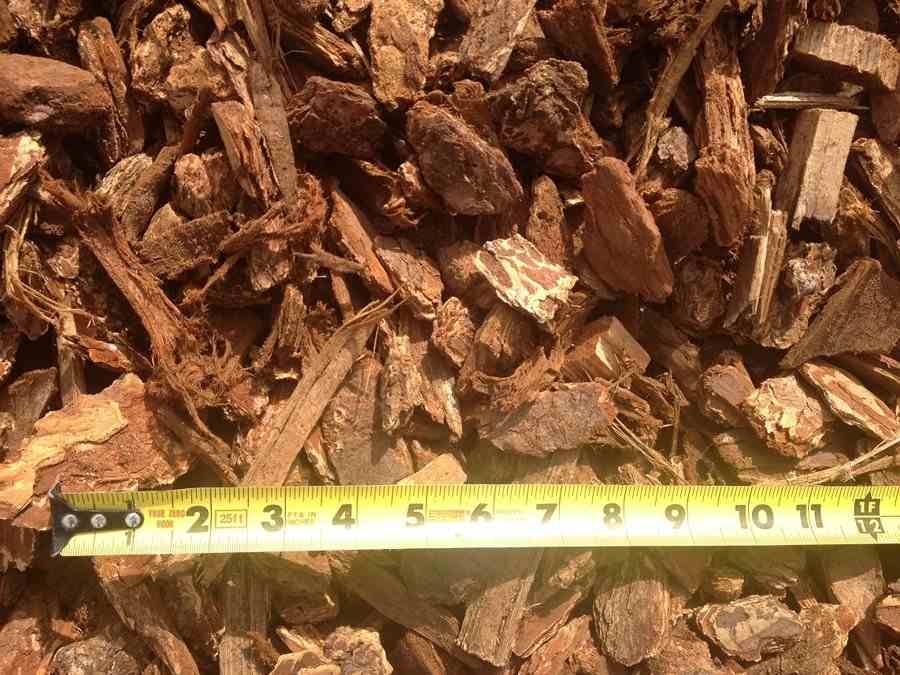 Pile of brown wood chips with a yellow measuring tape along the bottom edge.