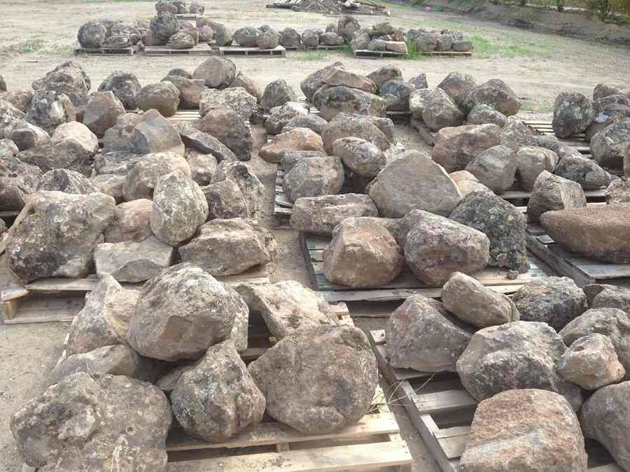Pile of large rocks on wooden pallets in an outdoor yard, with more stones stacked in the background