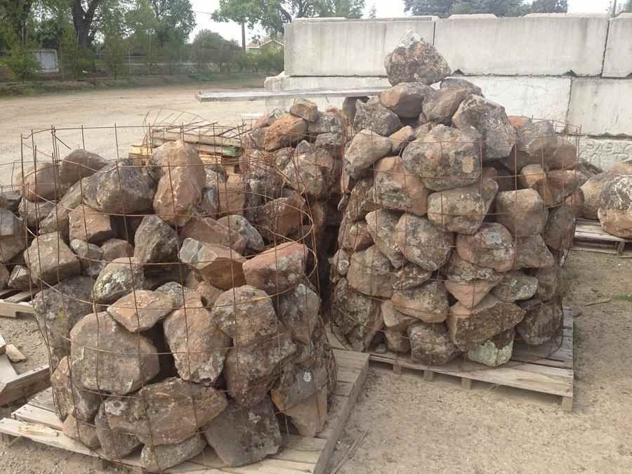 Piles of stacked rocks on wooden pallets outdoors near a concrete wall