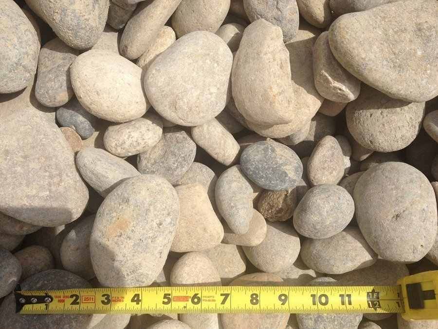Pile of smooth beige and gray pebbles with a yellow measuring tape along the bottom edge