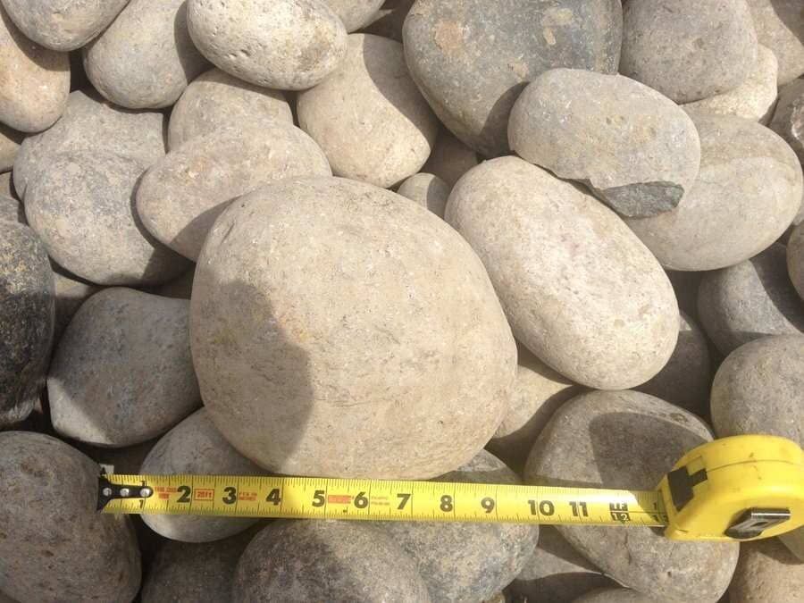 Yellow measuring tape across a pile of smooth gray rocks and pebbles