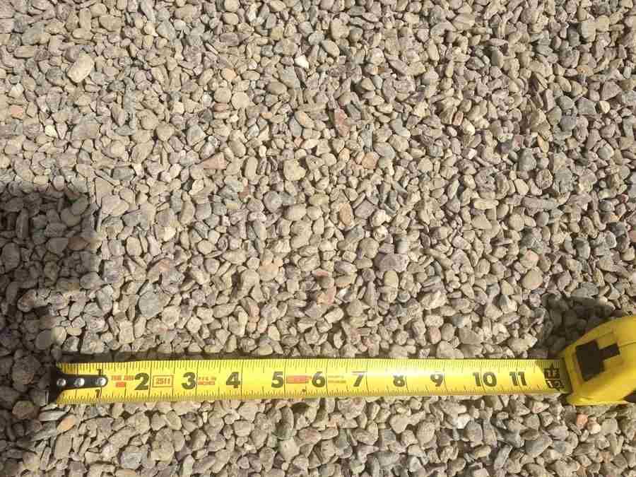 Yellow measuring tape laid across a bed of small tan gravel stones.