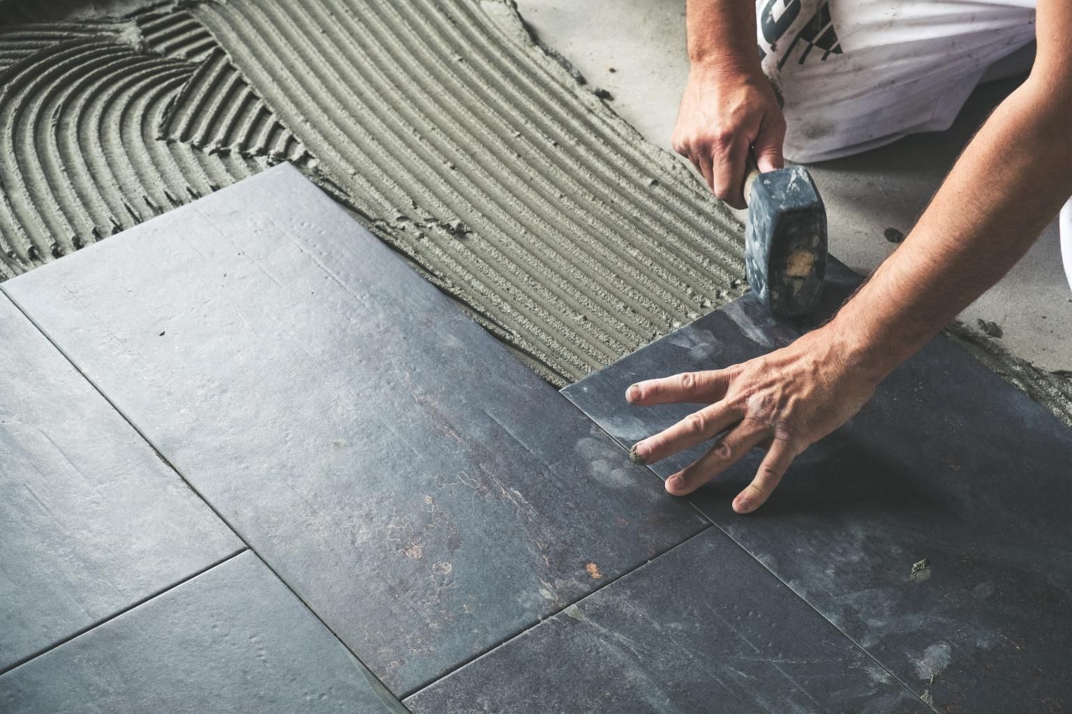 Worker installing dark floor tiles with a hand tool on a partially tiled surface
