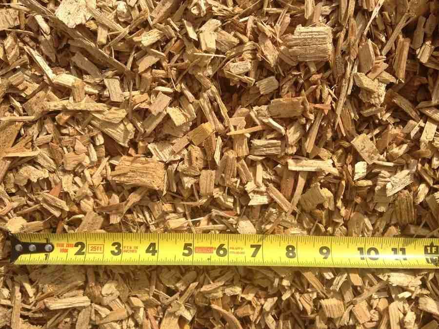 Wood chips piled above a yellow measuring tape showing inches along the bottom