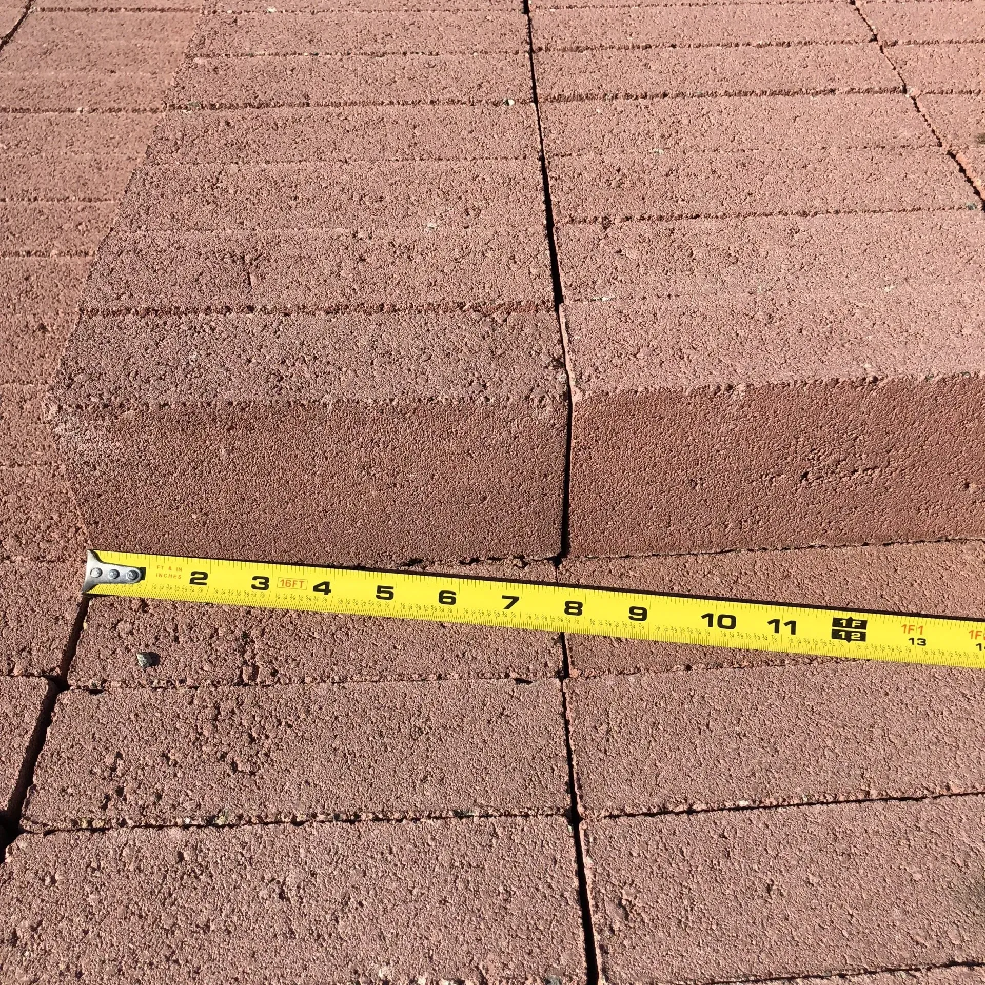 Yellow tape measure across a brown shingled roof, showing a visible seam or gap.